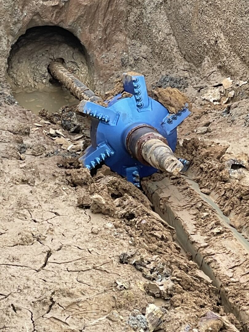 A blue pipe laying in the mud next to a hole.