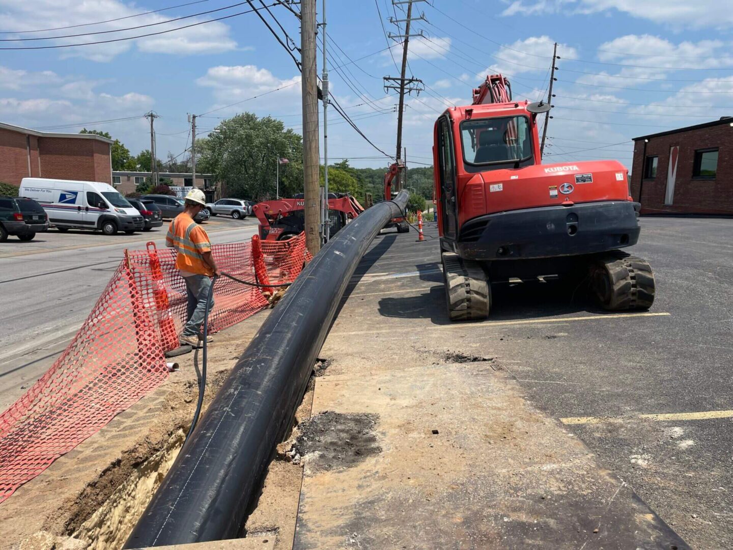 A man in an orange shirt is working on the side of a road.