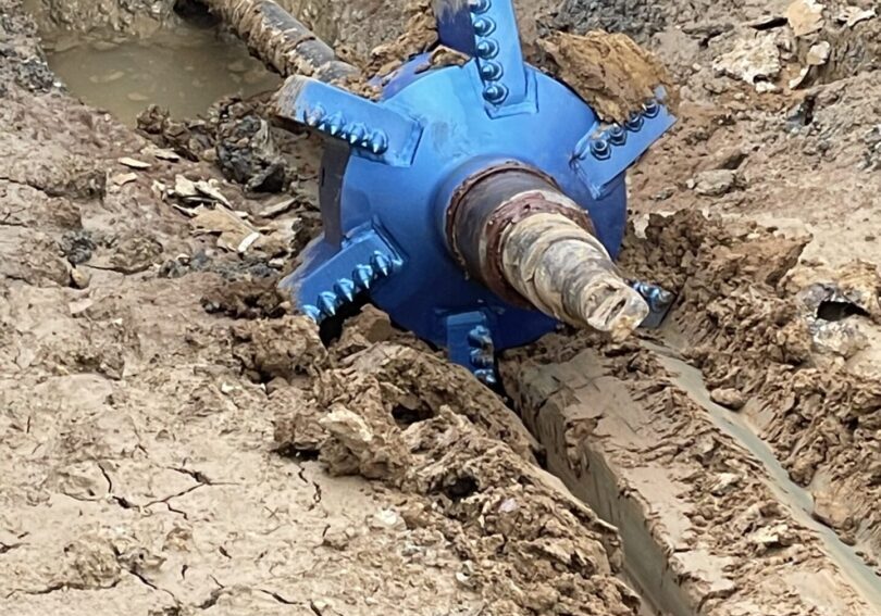 A blue pipe laying in the mud next to a hole.